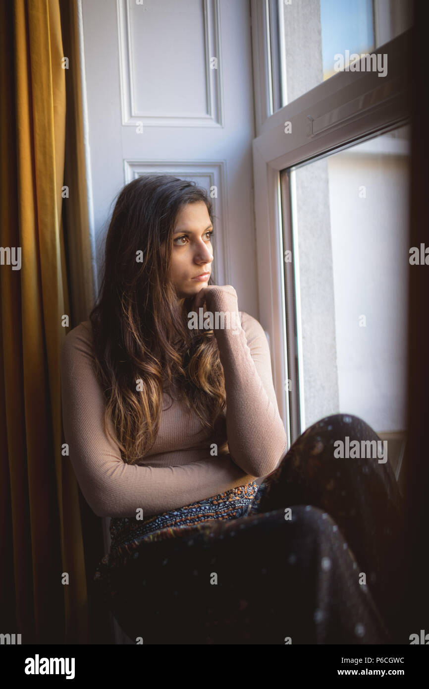 Femme à la fenêtre par while sitting on window sill Banque D'Images