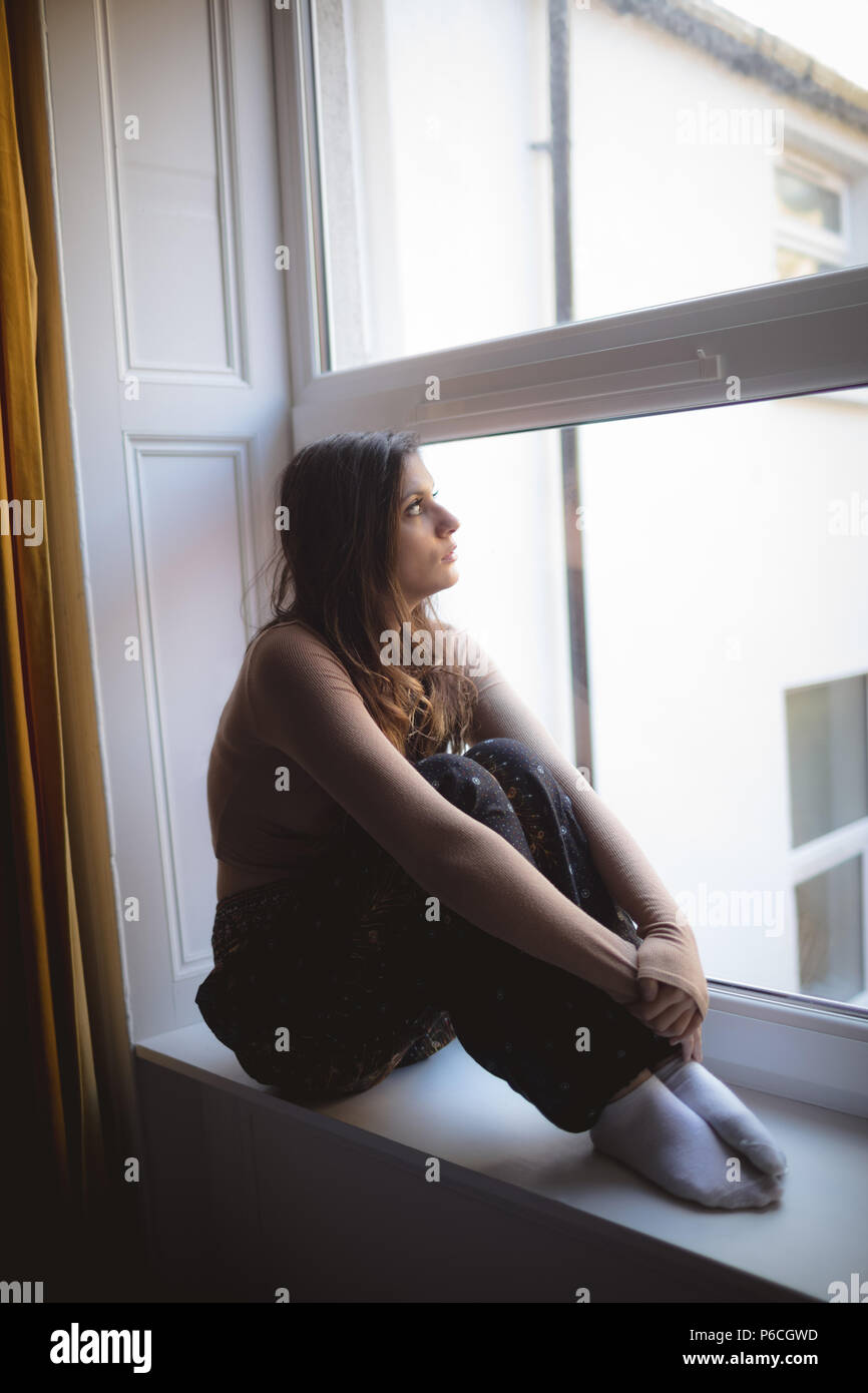Femme à la fenêtre par while sitting on window sill Banque D'Images