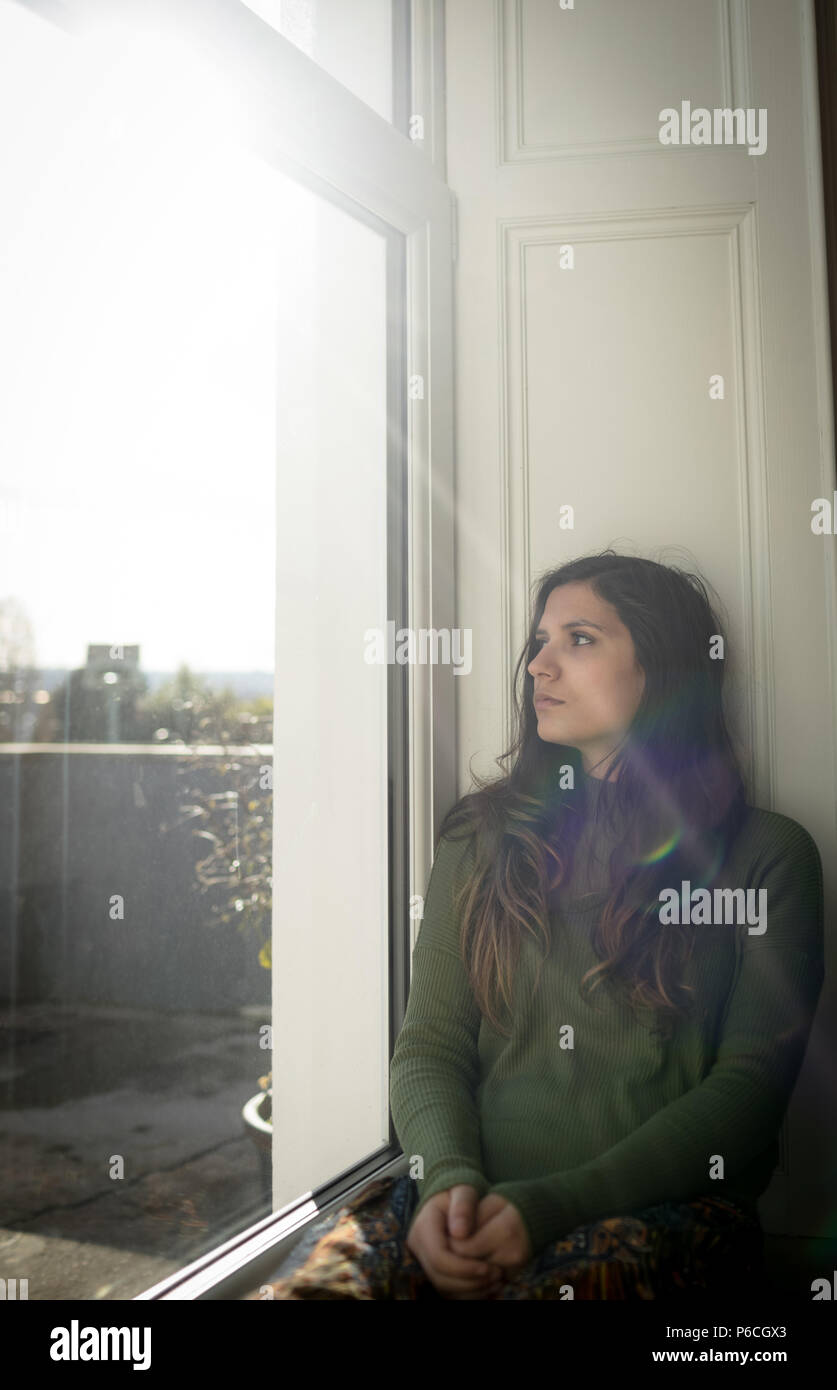 Femme à la fenêtre par while sitting on window sill Banque D'Images