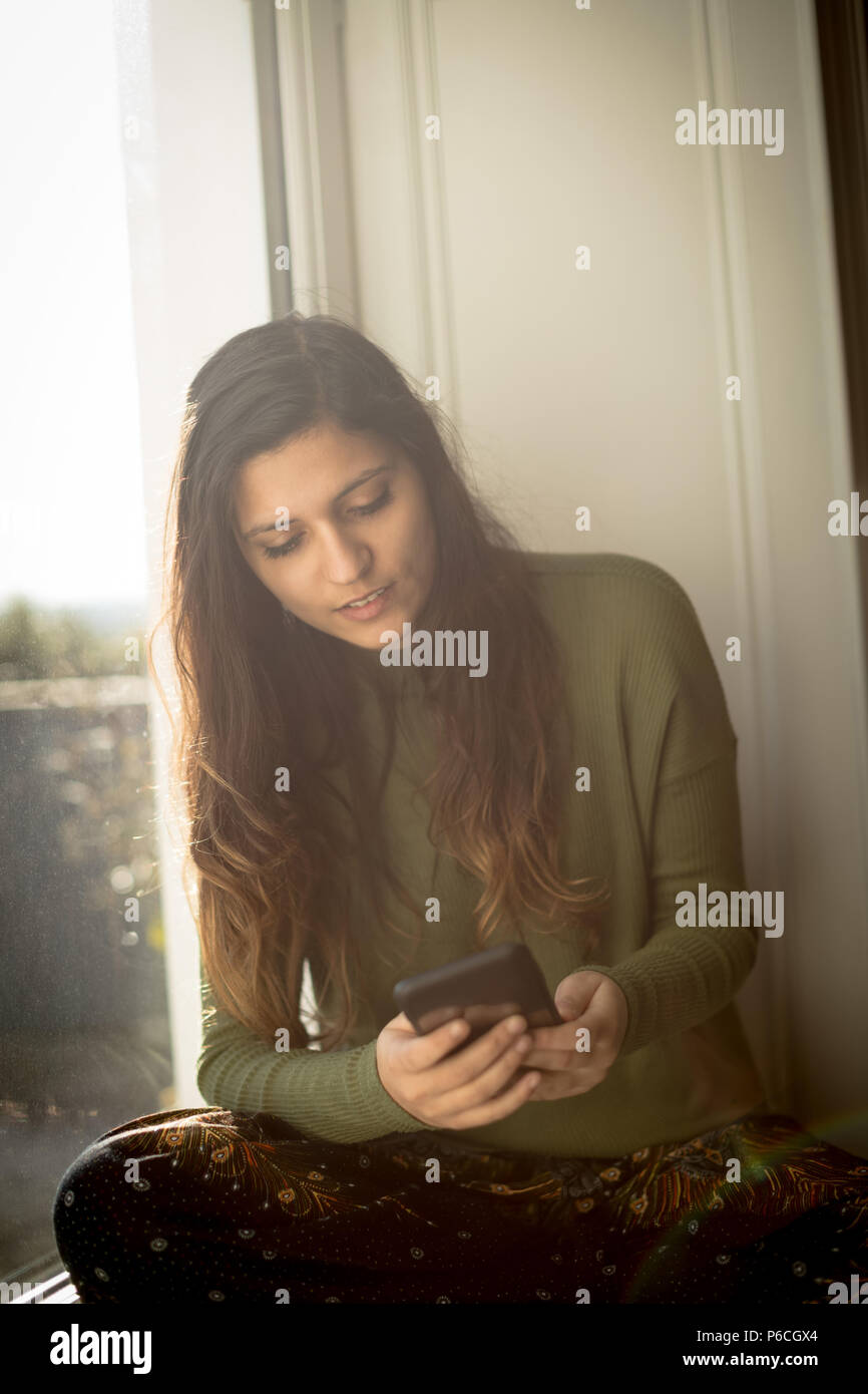 Woman using mobile phone sur à la maison Banque D'Images