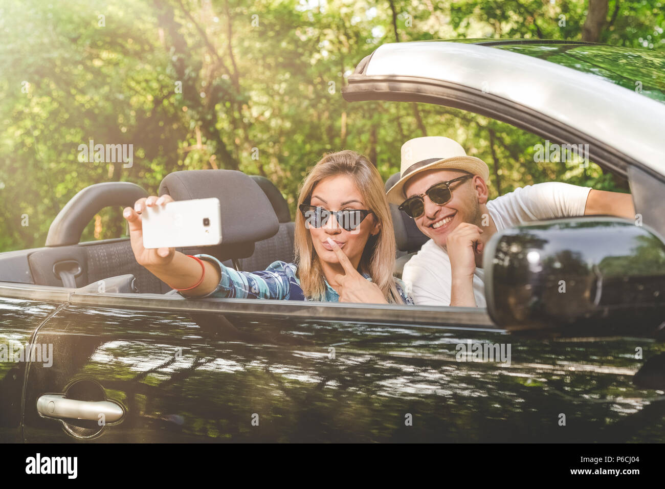 Couple avec smartphone selfies en position assise, dans une voiture décapotable. Concepts de la technologie et de voyage. Banque D'Images