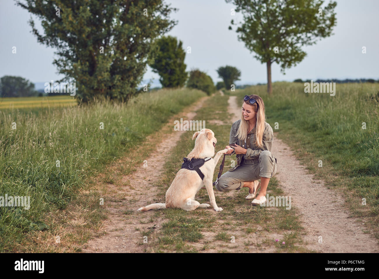Jeune femme aimant offert une patte par son chien alors qu'elle s'accroupit sur une route de campagne à la campagne durant leur promenade quotidienne Banque D'Images