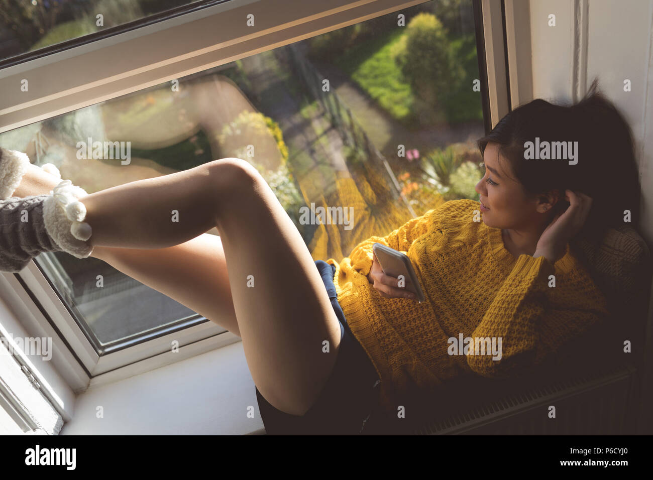 Femme à l'aide de fenêtre près de téléphone mobile Banque D'Images