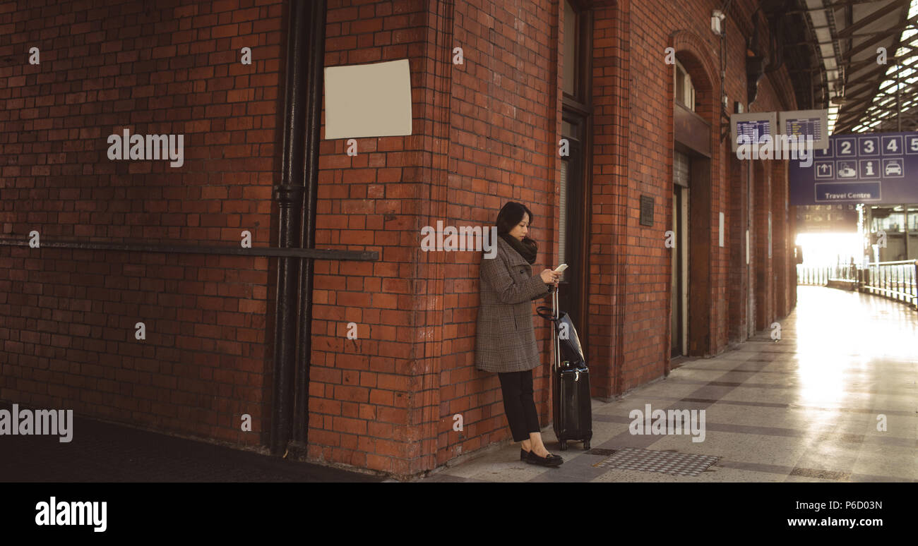 Femme à l'aide de téléphone mobile contre un mur de briques Banque D'Images