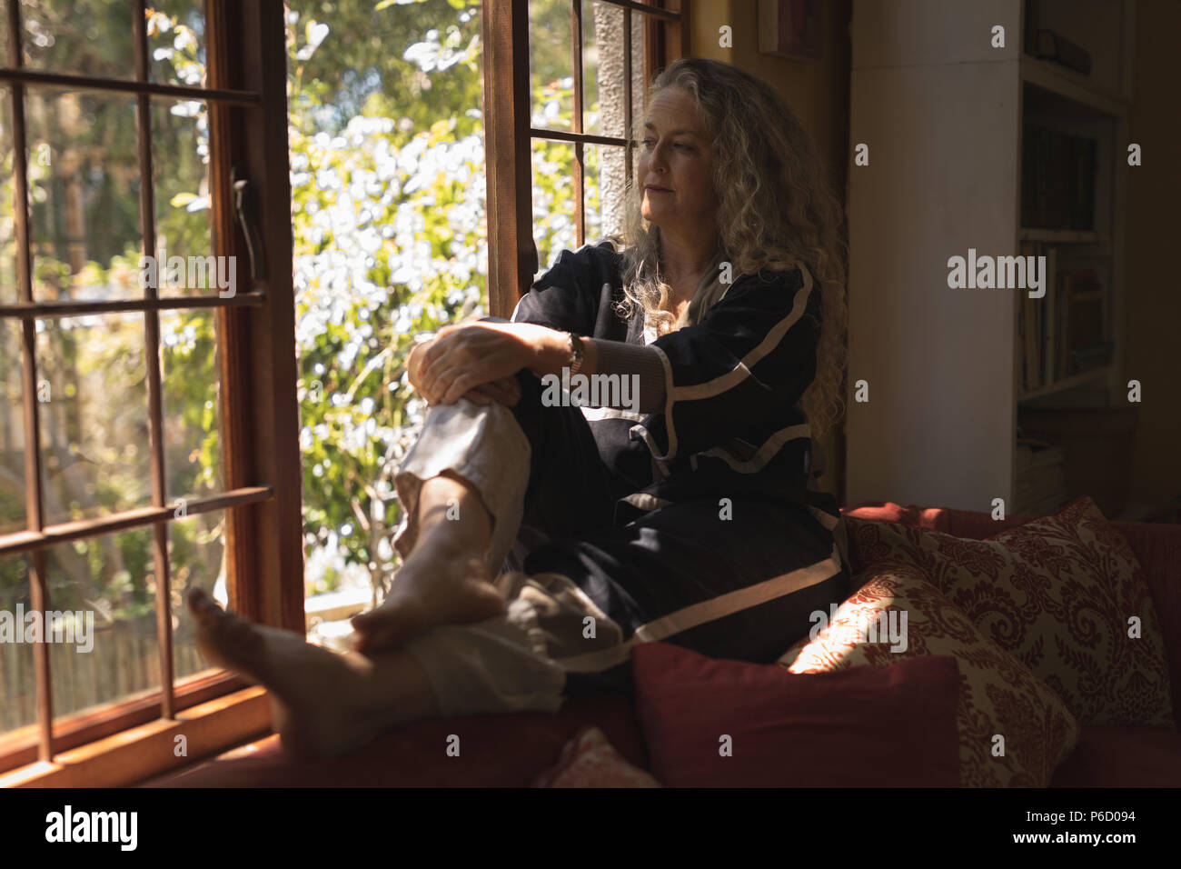Thoughtful mature woman sitting on windowsill Banque D'Images