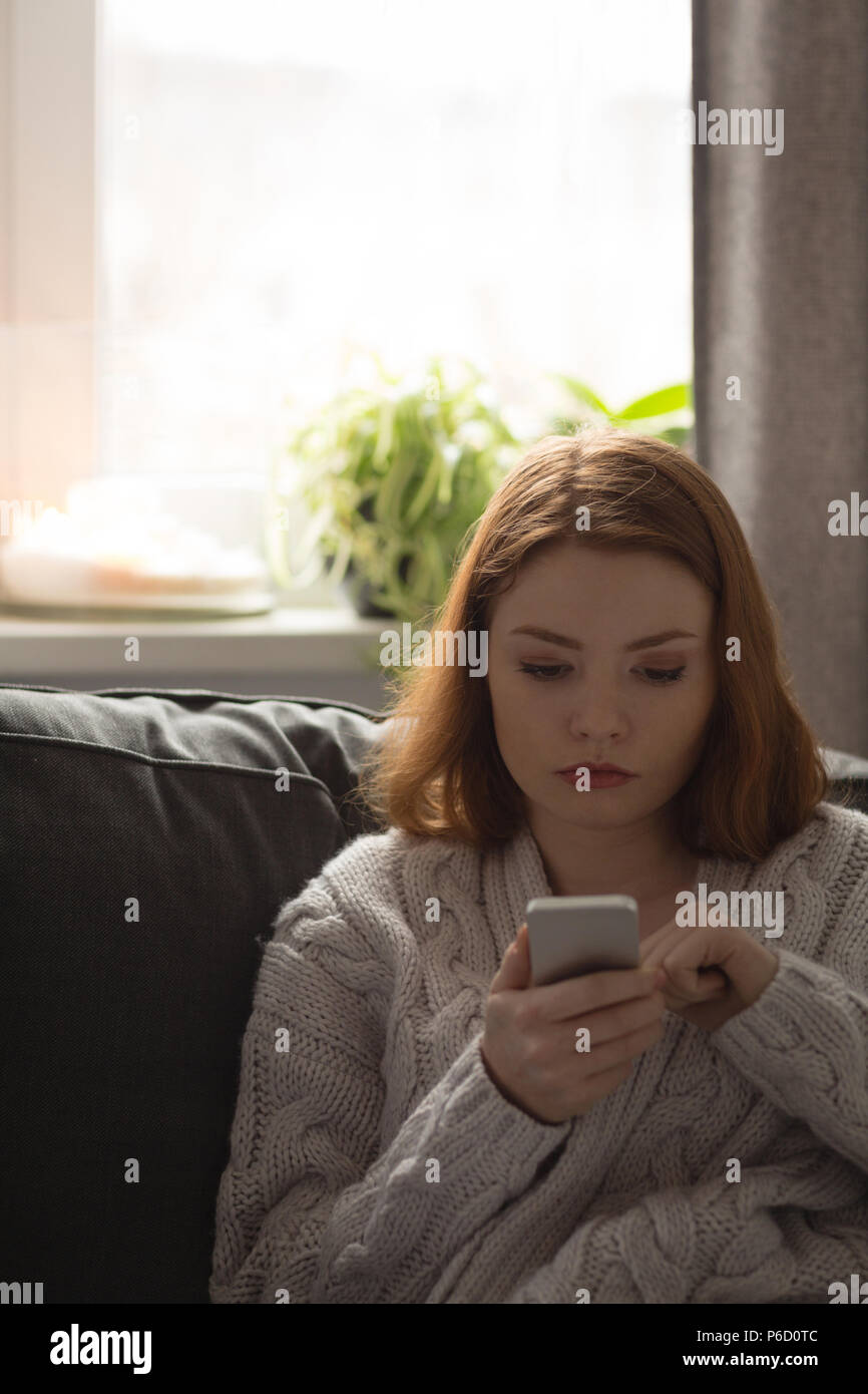 Woman using mobile phone in living room Banque D'Images