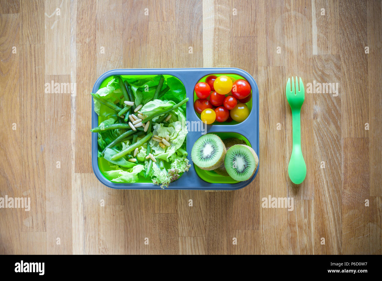 Silicone pliable boîte à lunch avec des aliments (salades vertes, tomates, kiwi) on wooden table Banque D'Images