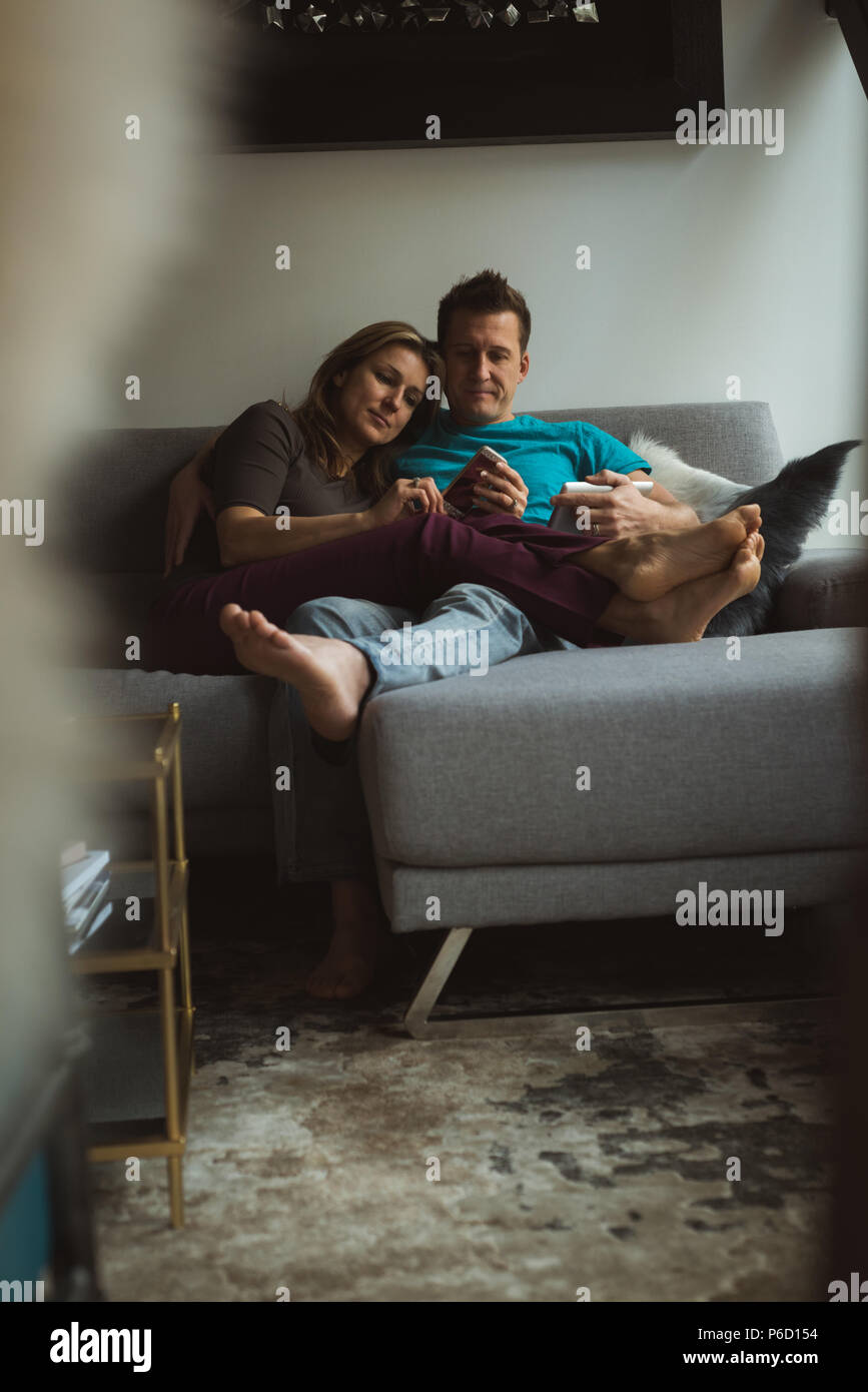 Couple à l'aide de téléphone mobile et tablette numérique dans la salle de séjour Banque D'Images