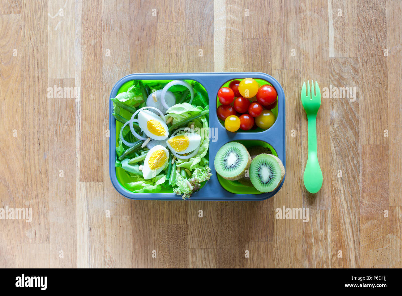 Silicone pliable boîte à lunch avec des aliments (salades vertes, des oeufs, des tomates, kiwi) on wooden table Banque D'Images