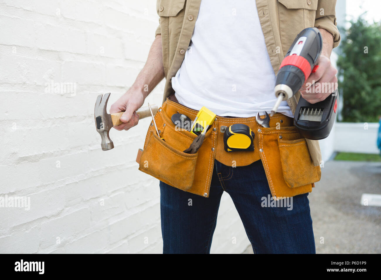 Male carpenter avec ceinture d'outils holding hammer et drill machine Banque D'Images