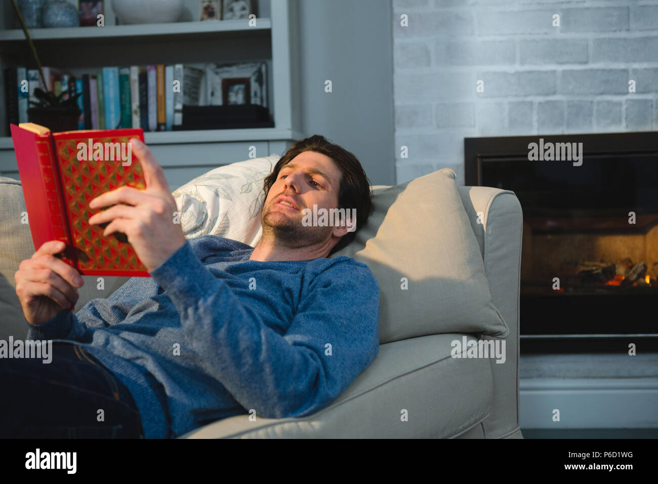 Man reading a book while lying on sofa in living room Banque D'Images