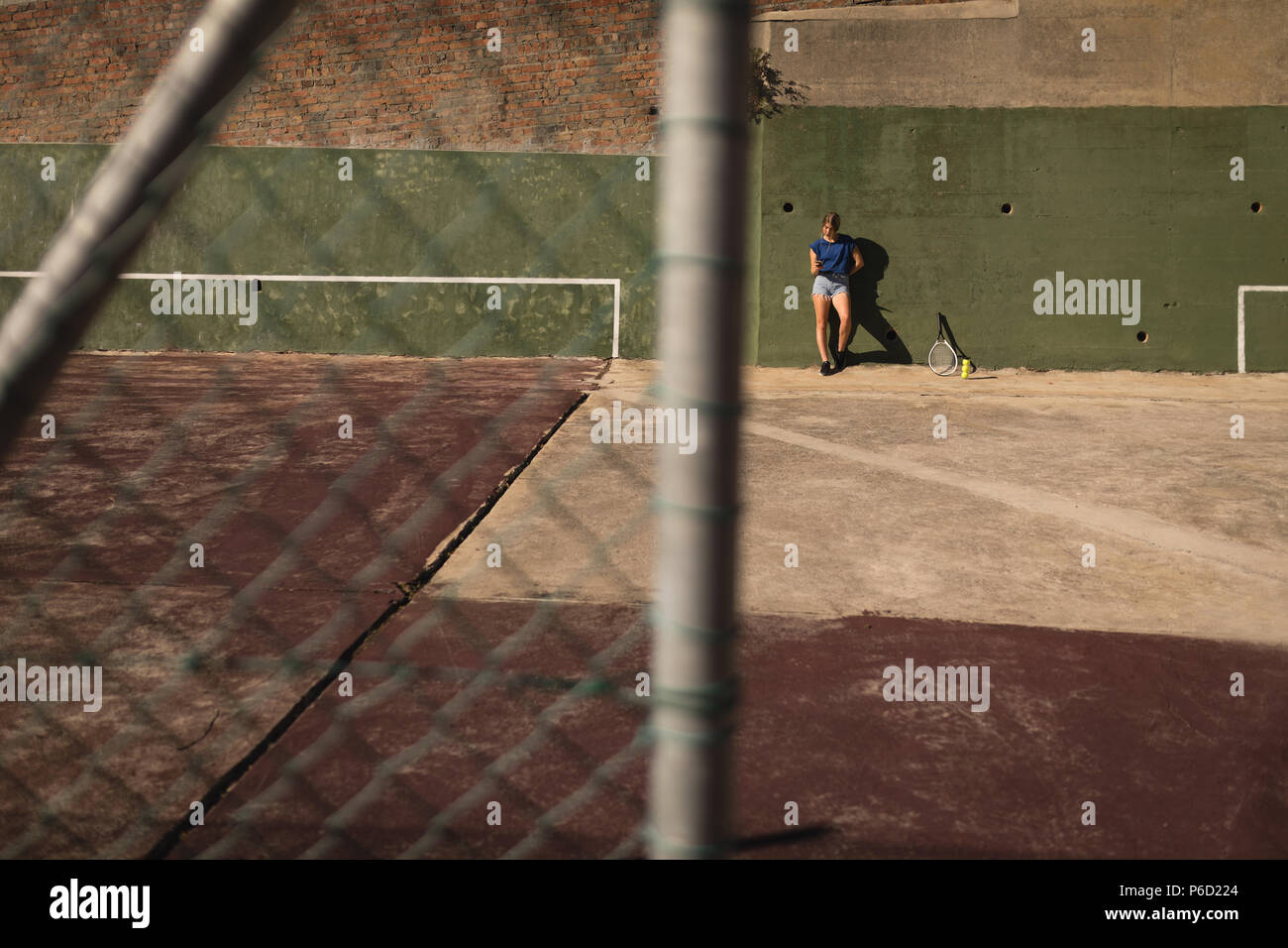 Woman leaning against wall dans la cour de tennis Banque D'Images