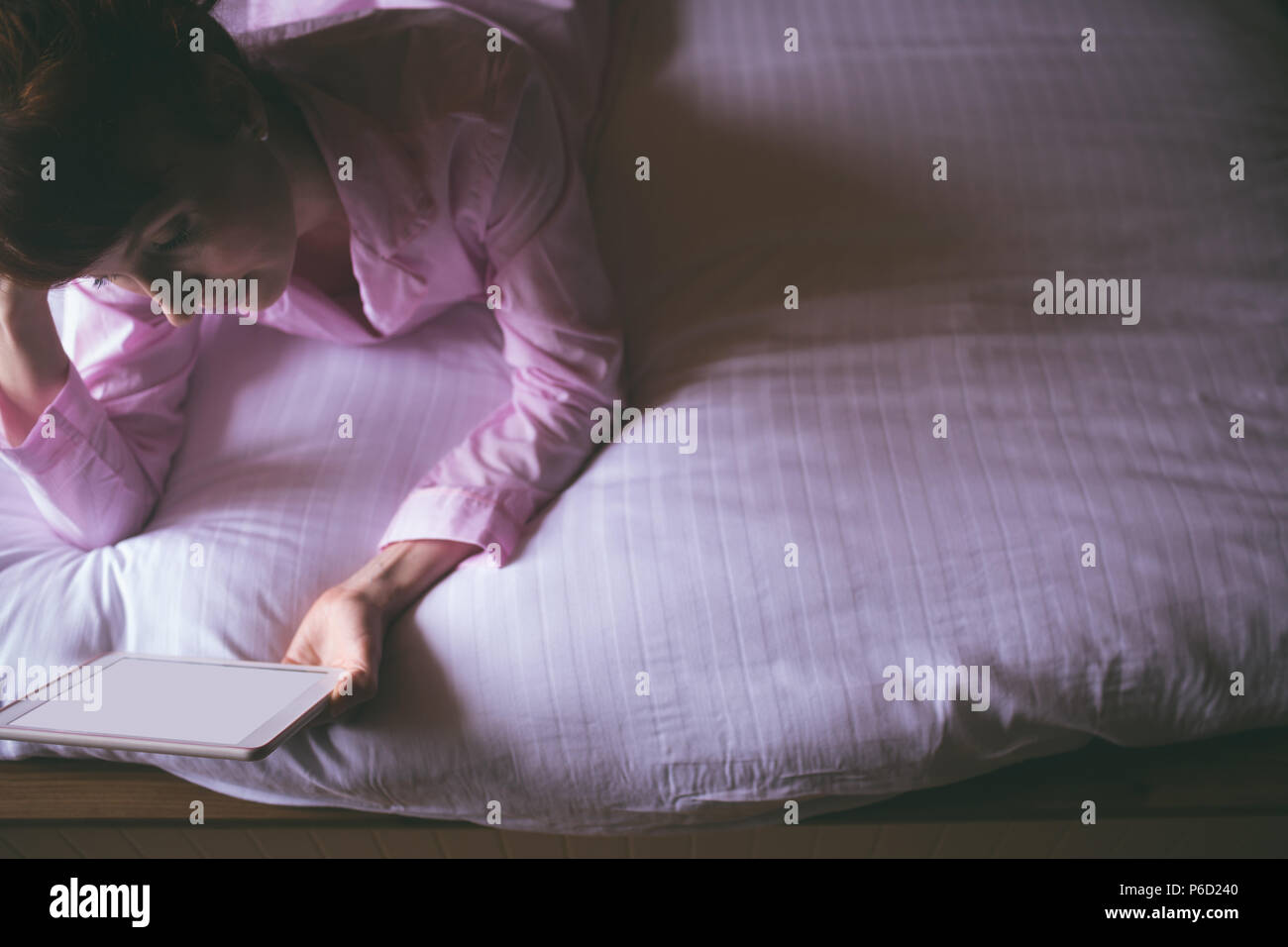 Woman using digital tablet while lying on lit dans la chambre Banque D'Images
