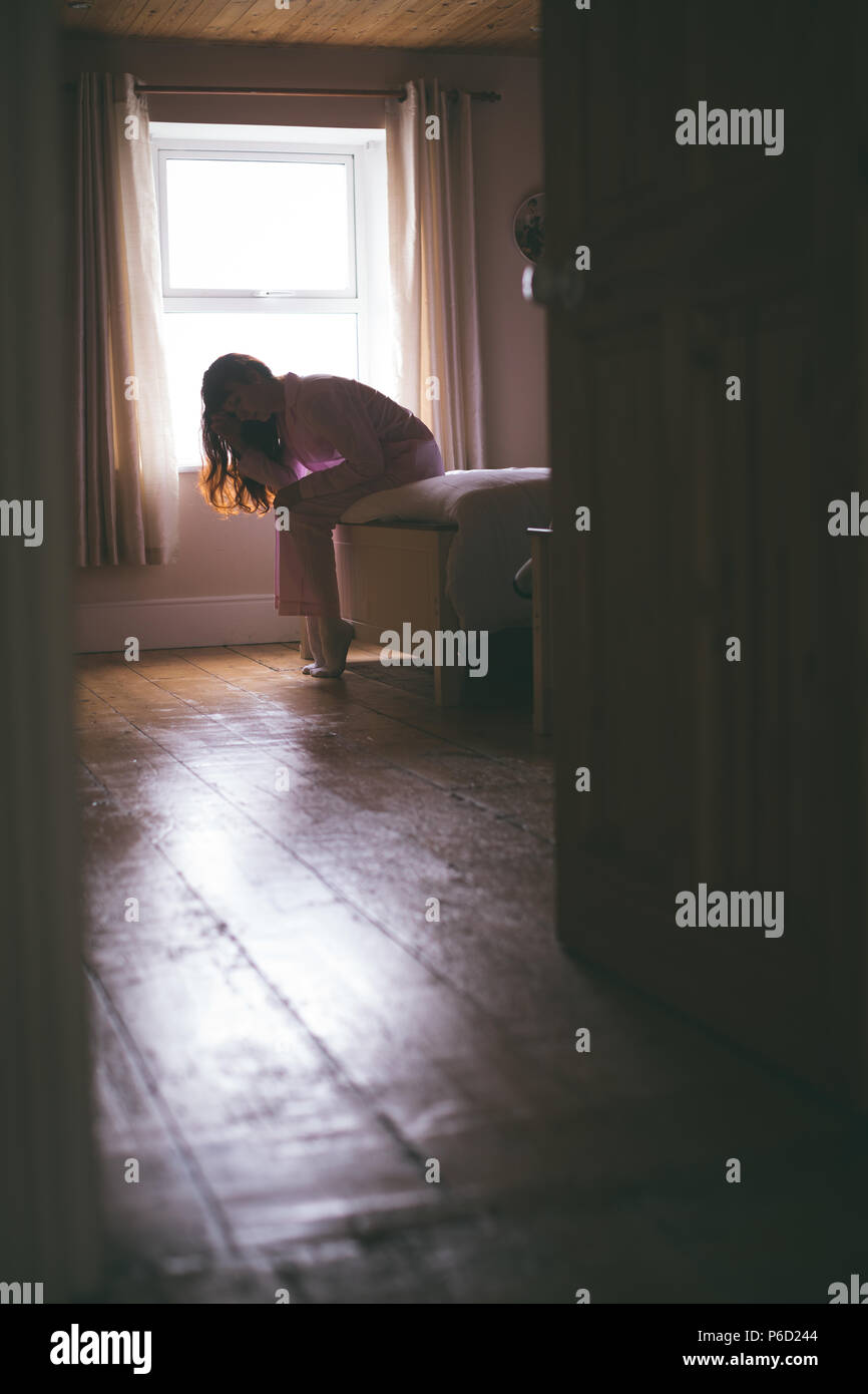 Femme assise tendue sur le lit dans la chambre Banque D'Images