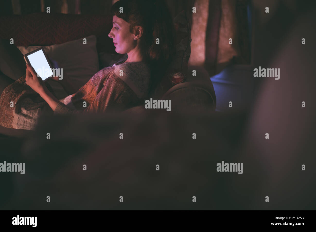 Woman using digital tablet on sofa in living room Banque D'Images
