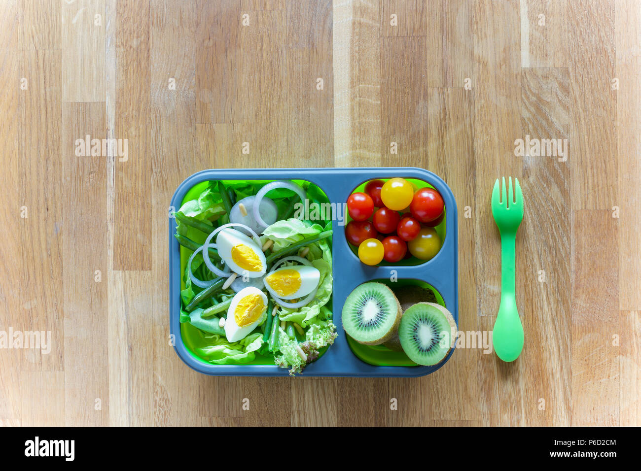 Silicone pliable boîte à lunch avec des aliments (salades vertes, des oeufs, des tomates, kiwi) on wooden table Banque D'Images