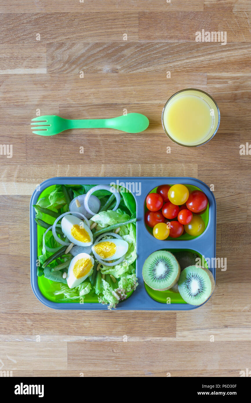 Silicone pliable boîte à lunch avec des aliments (salades, œufs, kiwi) sur table en bois et le jus d'orange Banque D'Images