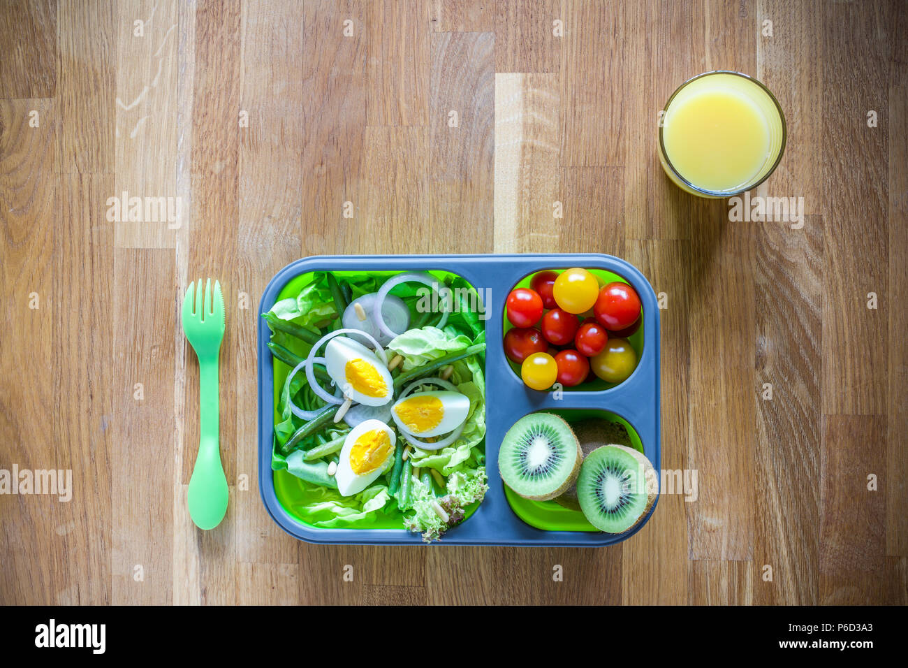 Silicone pliable boîte à lunch avec des aliments (salades, œufs, kiwi) sur table en bois et le jus d'orange Banque D'Images