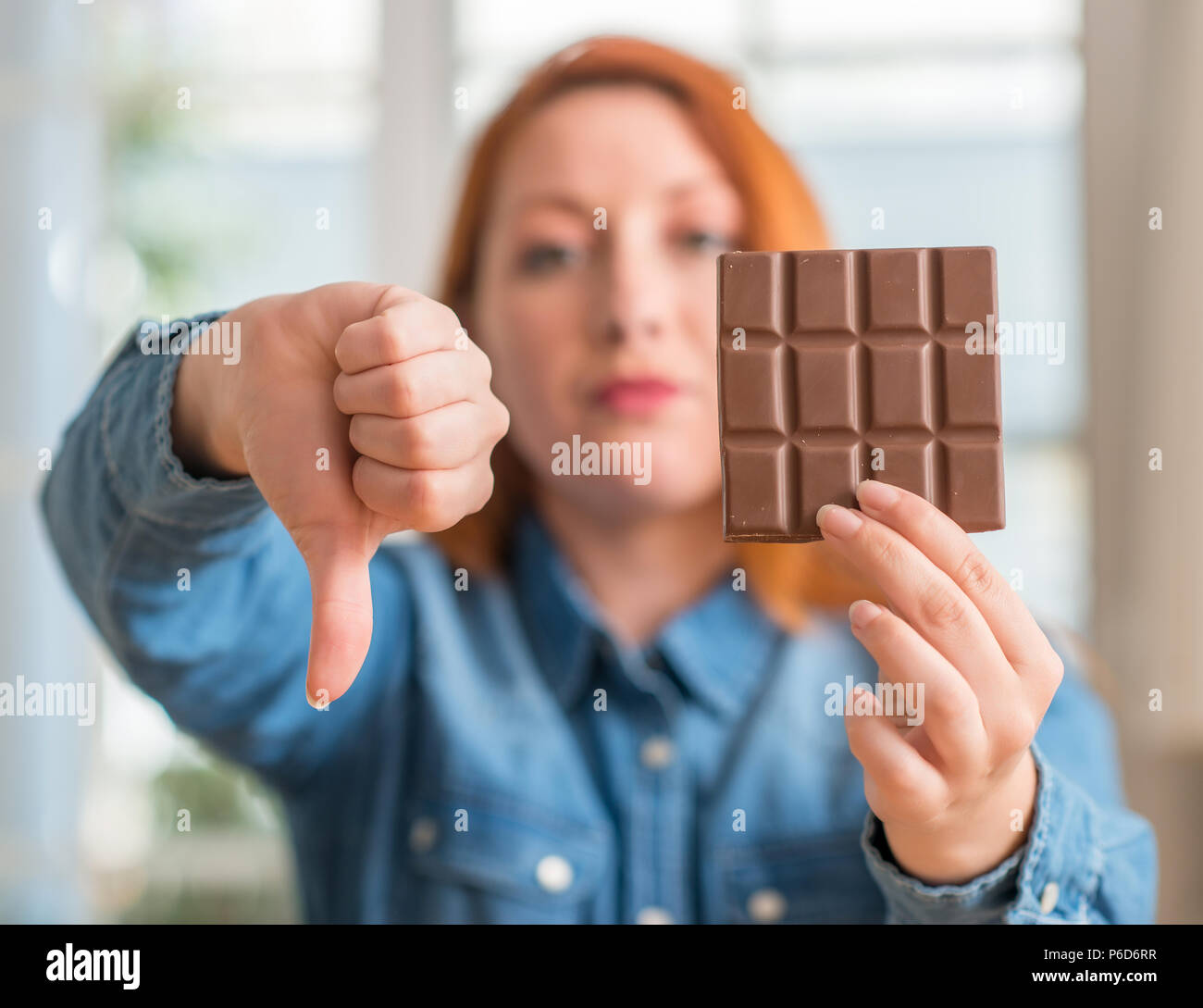 Redhead woman holding barre de chocolat à la maison, visage en colère avec signe négatif montrant non avec vers le bas, le rejet de la notion Banque D'Images