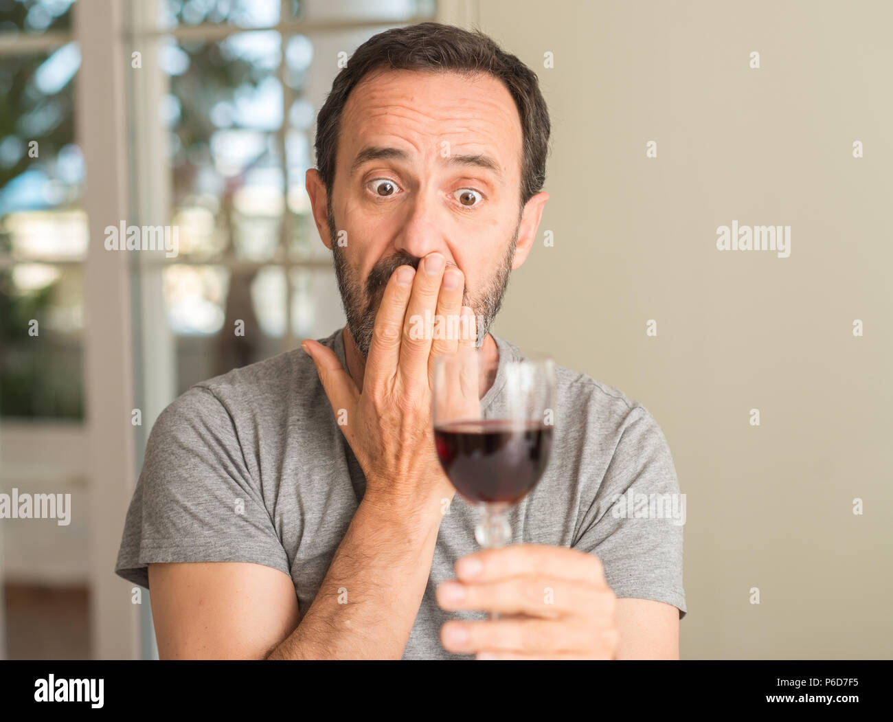 Homme d'âge moyen de boire un verre de vin couvrir la bouche à part choqué avec honte pour erreur, expression de la peur, peur en silence, concept secret Banque D'Images