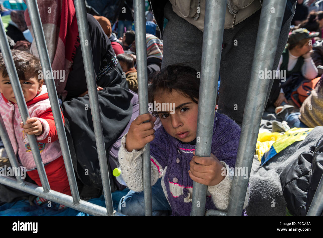 Fille de réfugiés derrière les garde-corps près de la porte pendant qu'ils attendent pour traverser la frontière au camp de réfugiés de fortune de la frontière près de l'Greek-Macedonian Banque D'Images