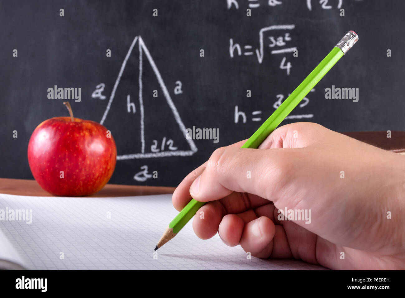 Male student part écrit dans le bloc-notes avec stylo en bois vert. Pomme Rouge et tableau noir est flou en arrière-plan. Concept de l'éducation et de classe Banque D'Images