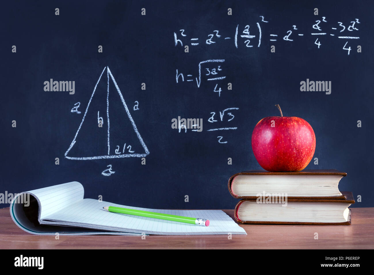 Livre vert sur Apple et stylo en bois ouverte sur l'ordinateur portable sur un bureau. Théorème de Pythagore écrit par la craie sur tableau noir. Classe de l'école et l'éducation Banque D'Images