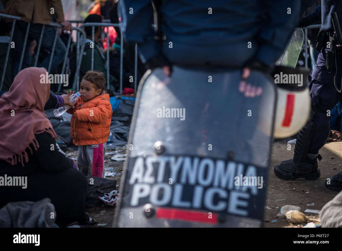 Mère donne à son enfant de boire de l'eau d'une bouteille près de la porte pendant qu'ils attendent pour traverser la frontière Greece-Macedonia au ca de réfugiés de fortune Banque D'Images