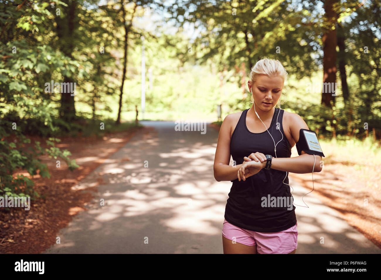 Fit young woman in sportswear, debout au milieu d'un chemin forestier de vérifier sa montre de sport avant d'aller pour une course Banque D'Images
