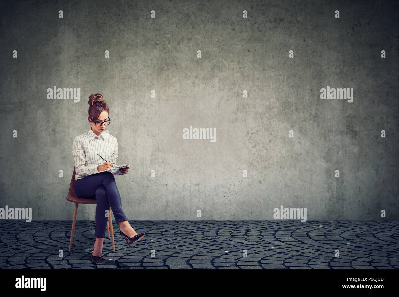 Femme élégante exerçant son activité et l'écriture sur le presse-papiers à remplir pour reprendre l'entrevue d'emploi tout en étant assis sur une chaise Banque D'Images