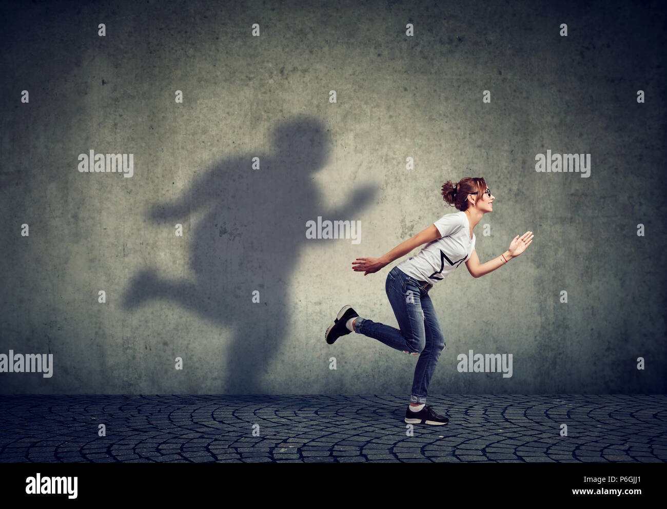 Femme courir loin de son ombre sur le mur de graisse. Contrôle de poids concept Banque D'Images