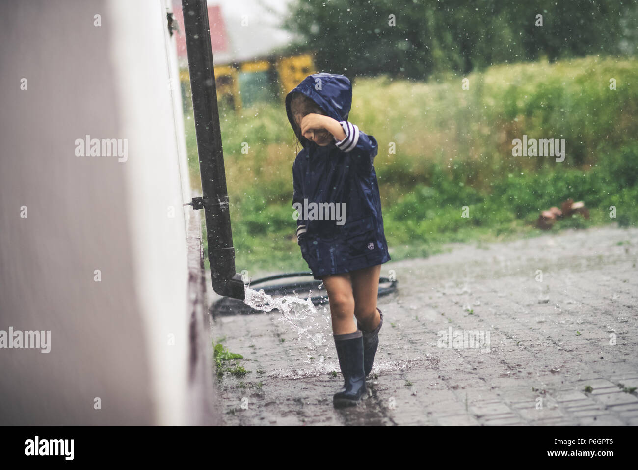 Petite fille jouant seul à l'extérieur par mauvais temps. Pluie d'été Banque D'Images