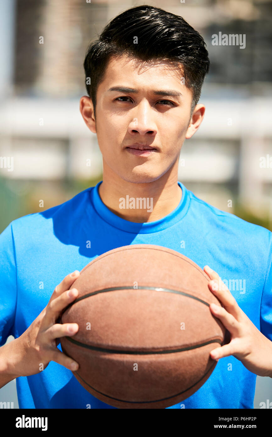 Les jeunes mâles d'Asie de basket-ball joueur tenant une boule en regardant la caméra. Banque D'Images
