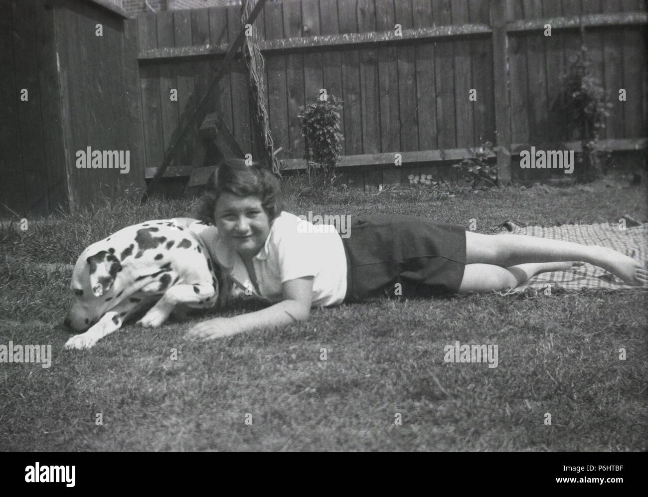 Années 1950, jeune écolière couché à l'extérieur dans un jardin sur un tapis avec son animal de compagnie chien Dalmatien. Un unique race tachetée, Dalamations sont de bons chiens de famille, être chaleureux, intelligent et ludique. Banque D'Images