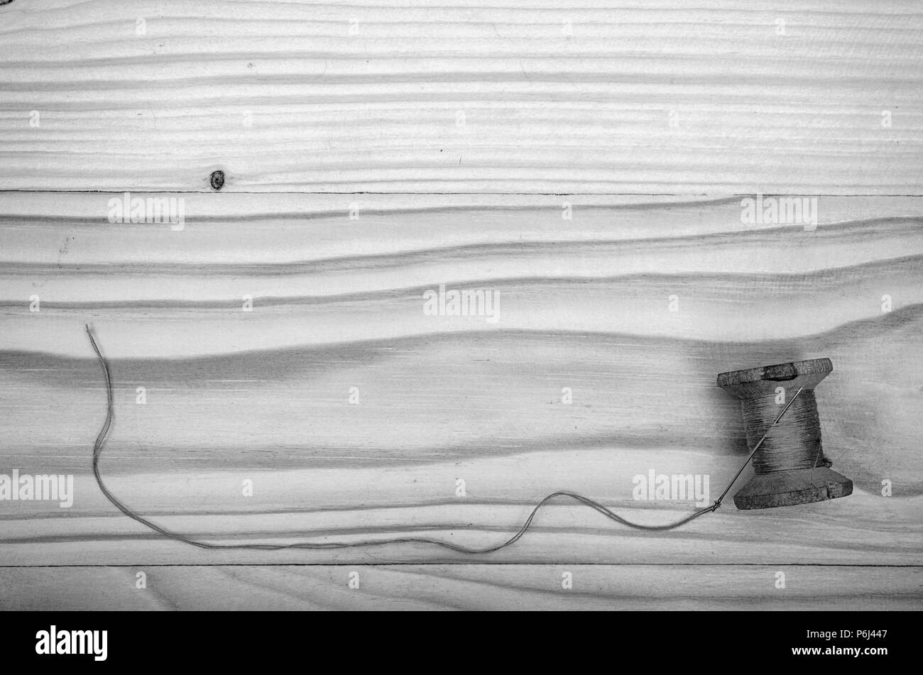 L'ancienne bobine de fil et une aiguille sur une table en bois en noir et blanc. Banque D'Images