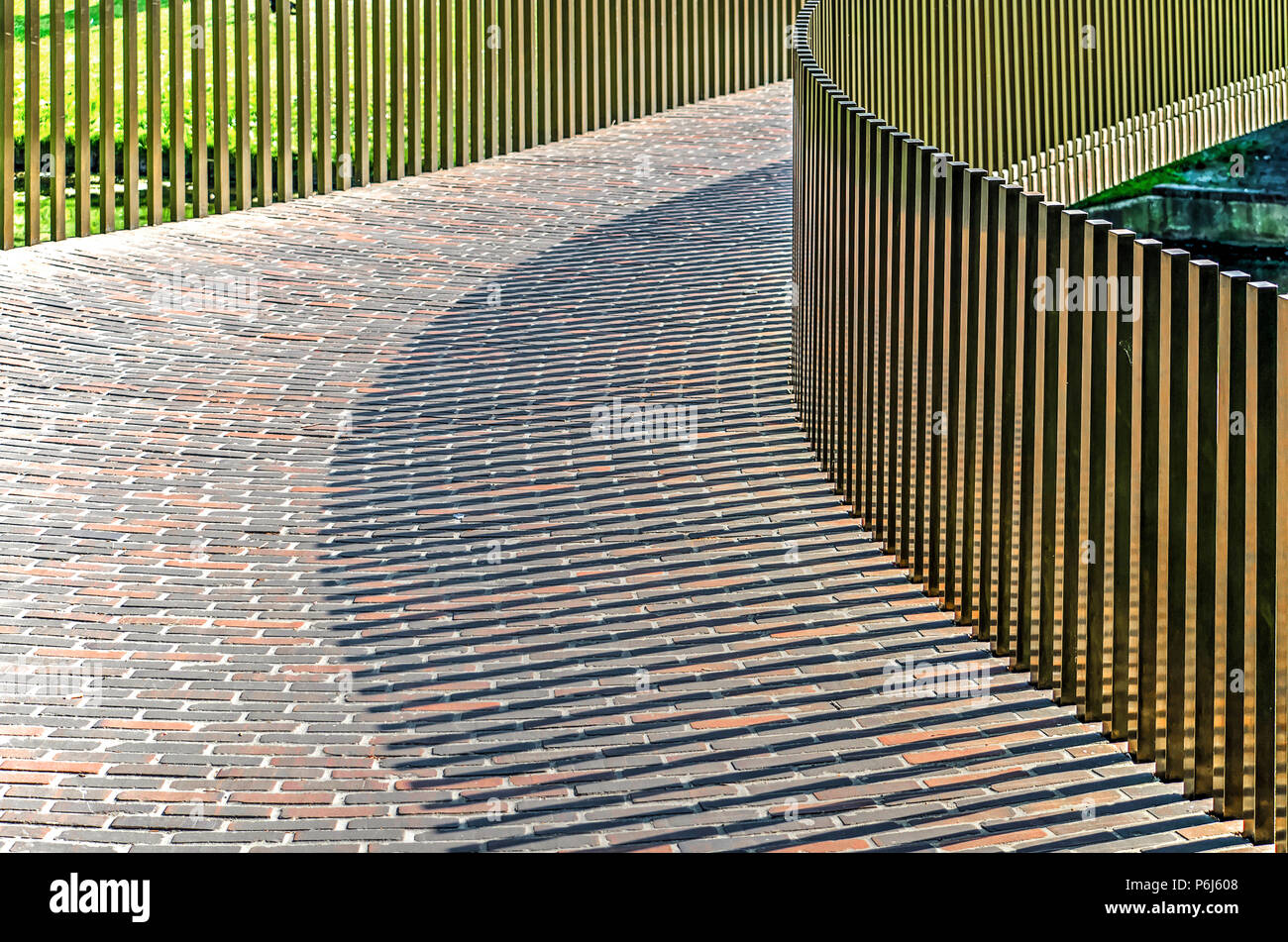 Rotterdam, Pays-Bas, le 20 mai 2018 : la balustrade en laiton jette des ombres sur le sol en brique de la passerelle pour piétons à travers Westersingel Banque D'Images