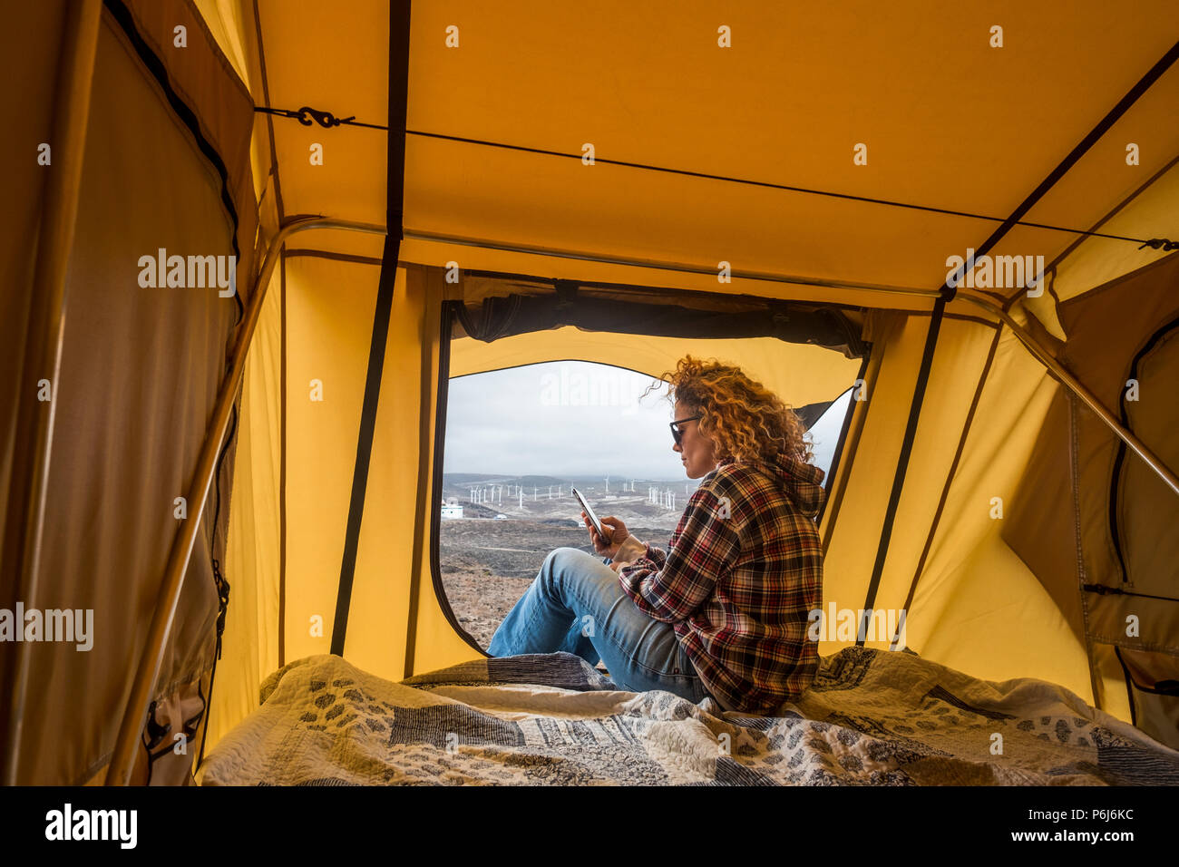 Belle caucasian woman vérifiez les contacts internet pour smartphone et travailler pendant que s'asseoir à l'extérieur d'une tente avec vue sur l'océan. Concept de déplacement et de travail w Banque D'Images