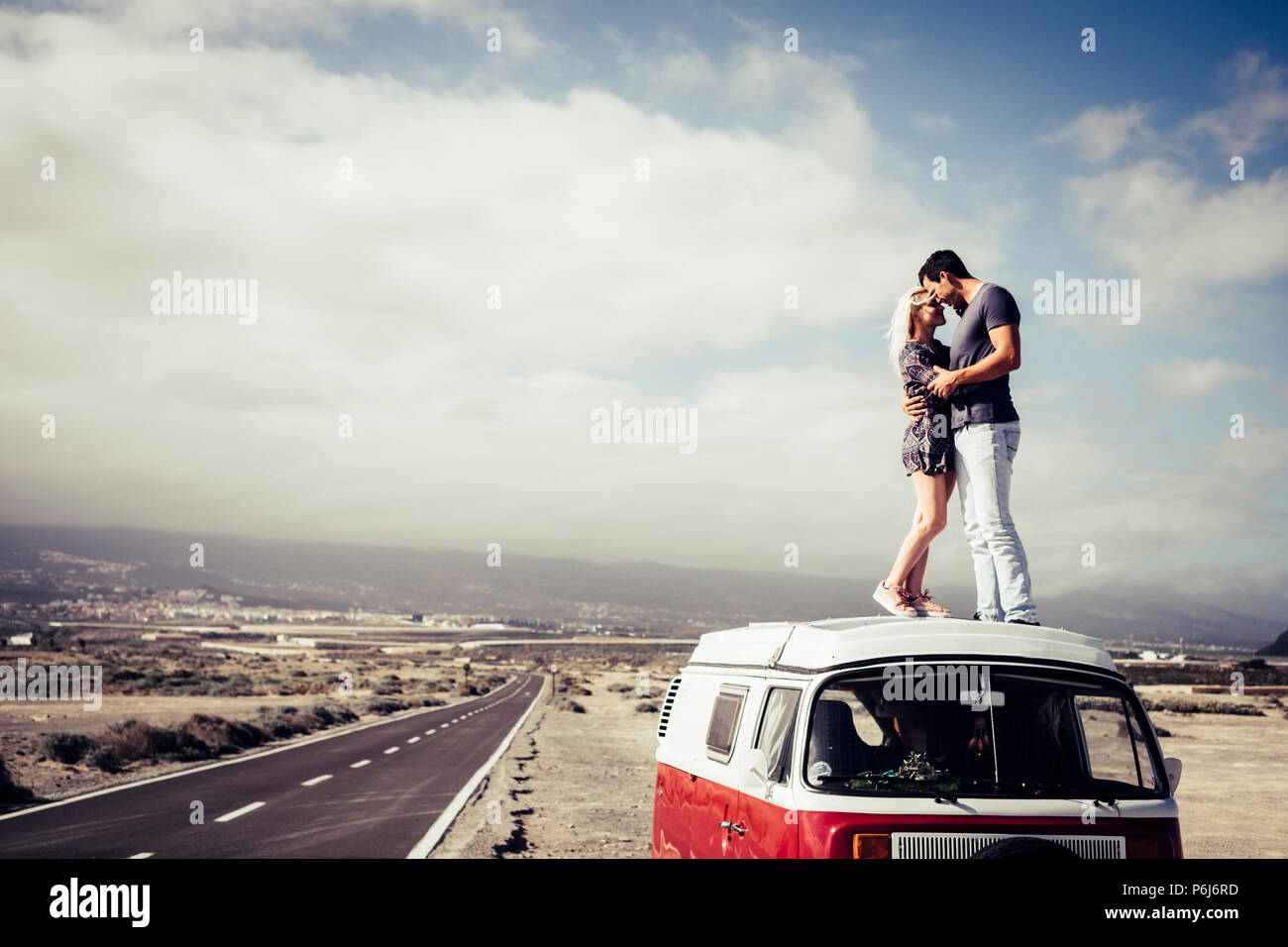 Beau couple dans l'amour debout sur le toit d'un van legendaru vintage. transport et notion de famille. longue route asphaltée en arrière plan et du ciel Banque D'Images