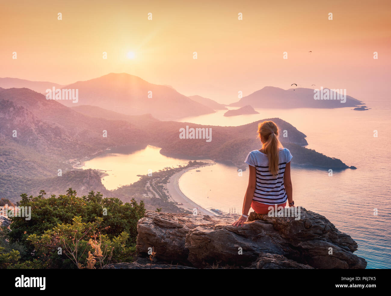 Jeune femme assise sur le haut du rocher et regardant la mer et les montagnes au soleil colorés en été. Paysage avec vue sur la mer, la montagne, fille ridg Banque D'Images