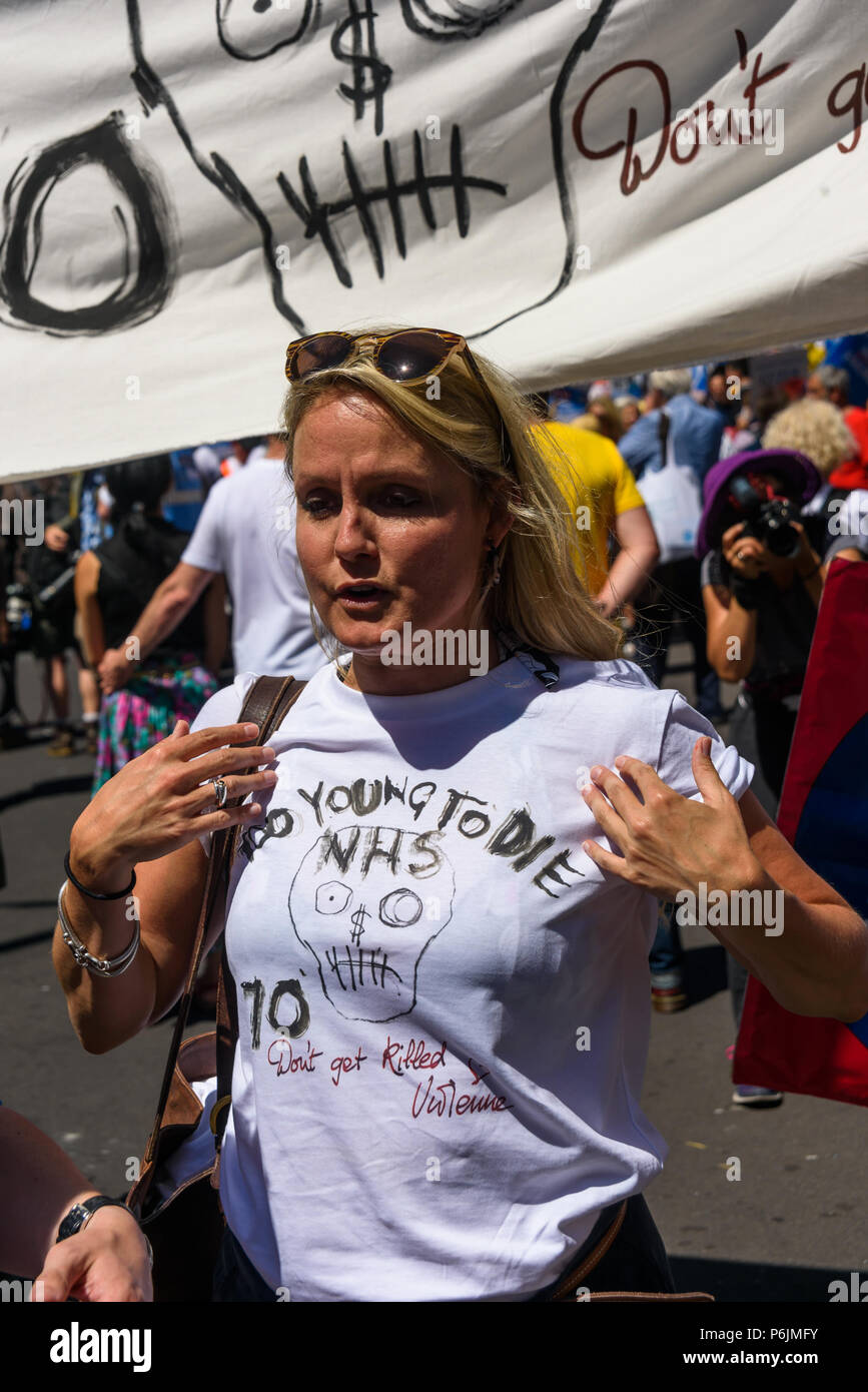 30 juin 2018 - Londres, Royaume-Uni. 30 juin 2018. Un médecin montre le t-shirt conçu par Vivienne Westwood pour le NHS 70e anniversaire avec le message "Trop jeune pour mourir" devant des milliers de mars à Londres à partir de la BBC pour un rassemblement près de Downing St pour célébrer 70 ans de l'ENM, et à l'appui de ses travailleurs dévoués pour exiger une société publique NHS c'est gratuit pour tous avec un financement et dotation appropriée et fournir des services de classe mondiale pour chaque communauté. La manifestation, organisée par le l'Assemblée du peuple, des campagnes de santé ensemble, Trades Union Congress, Unison, Unite, GMB, Britis Banque D'Images