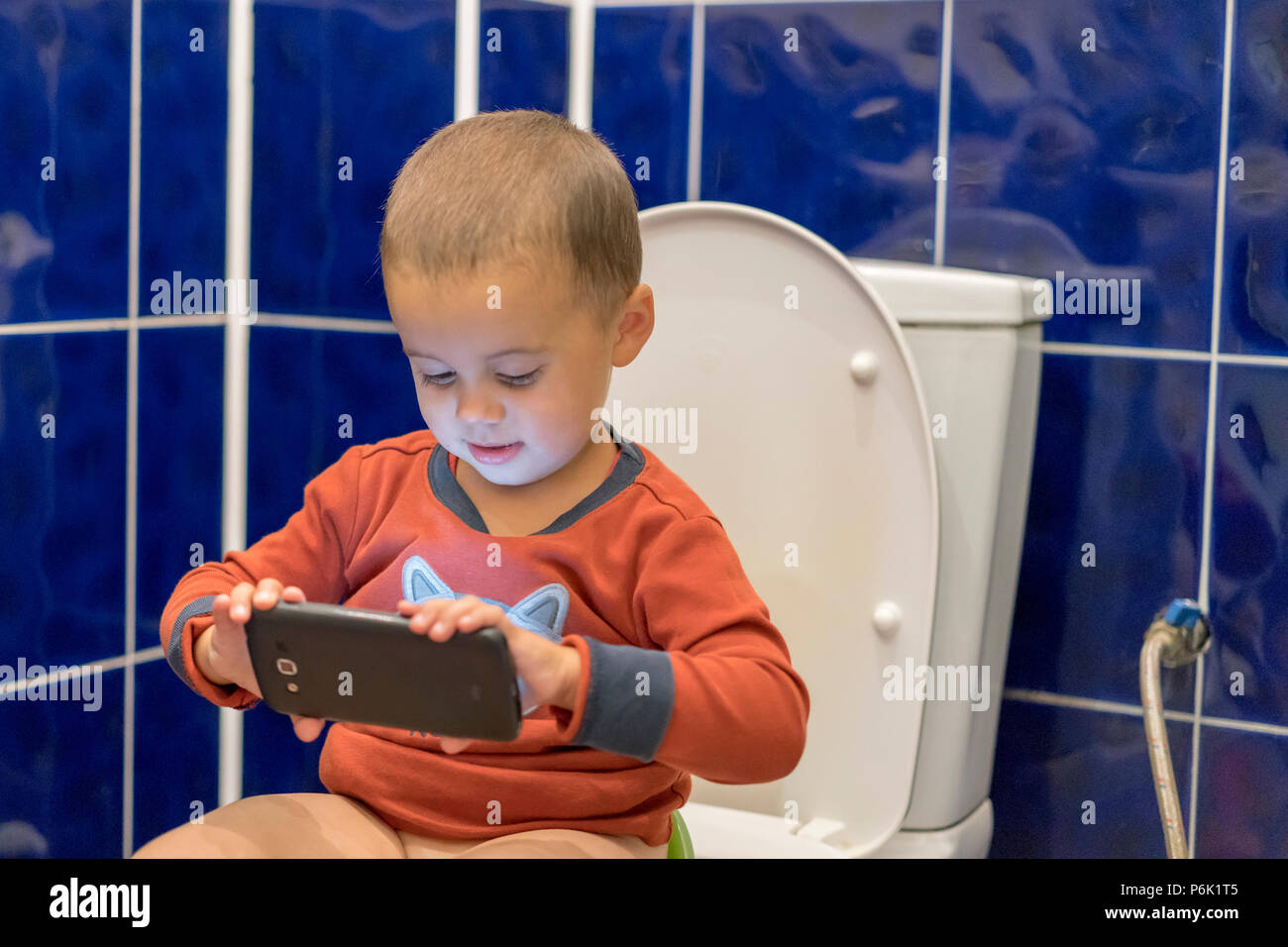 Mignon bébé garçon avec le smartphone dans la salle de bains. Petit garçon  assis sur les toilettes dans la salle de bains à la maison avec l'aide d'un  smartphone. Bébé garçon sittin