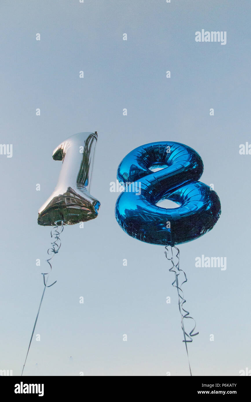 Deux ballons d'hélium pour célébrer un 18e anniversaire partie contre un ciel bleu au crépuscule Banque D'Images