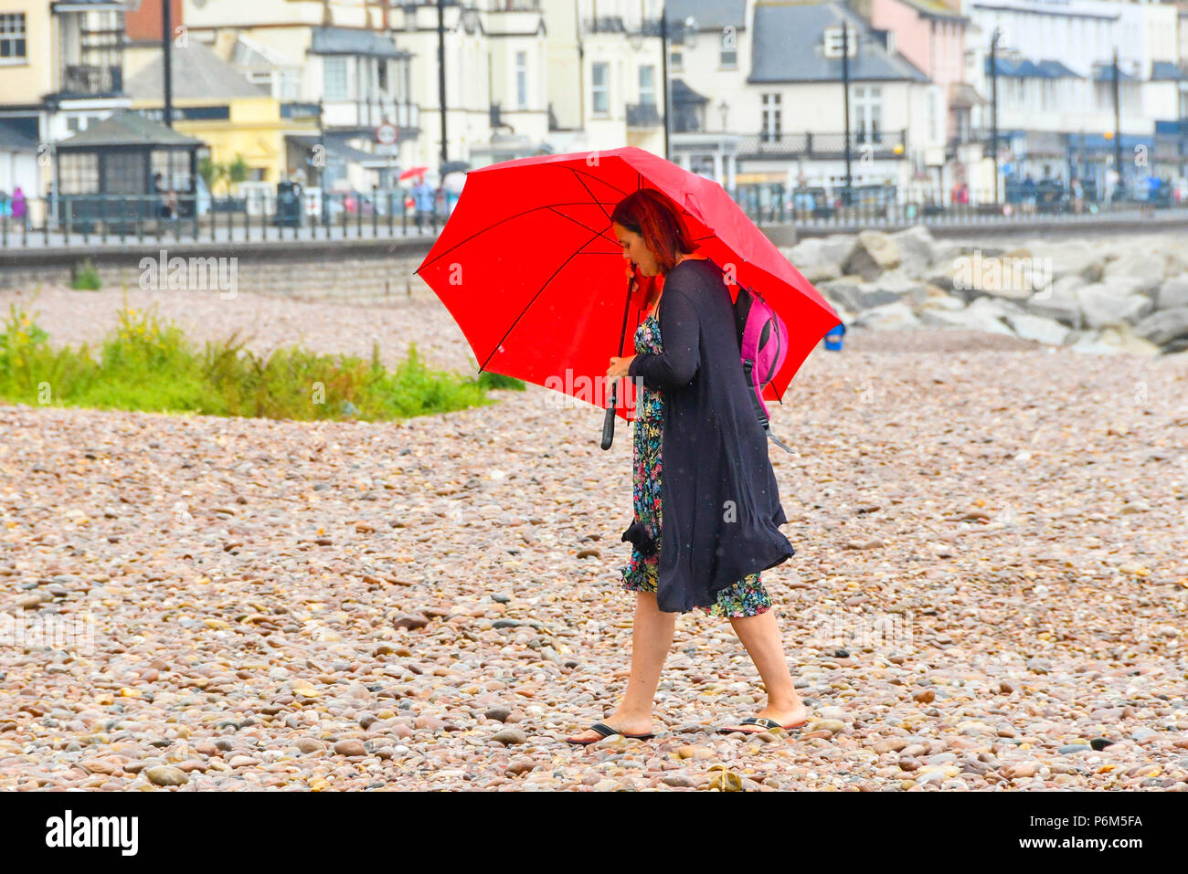 La ville de Sidmouth, Devon, UK. 1er juillet 2018. Météo britannique. Une femme sur la plage à la station balnéaire de Sidmouth dans le Devon avec parapluie comme la ville attrape le bord d'une adoption forte pluie douche. Crédit photo : Graham Hunt/Alamy Live News Banque D'Images