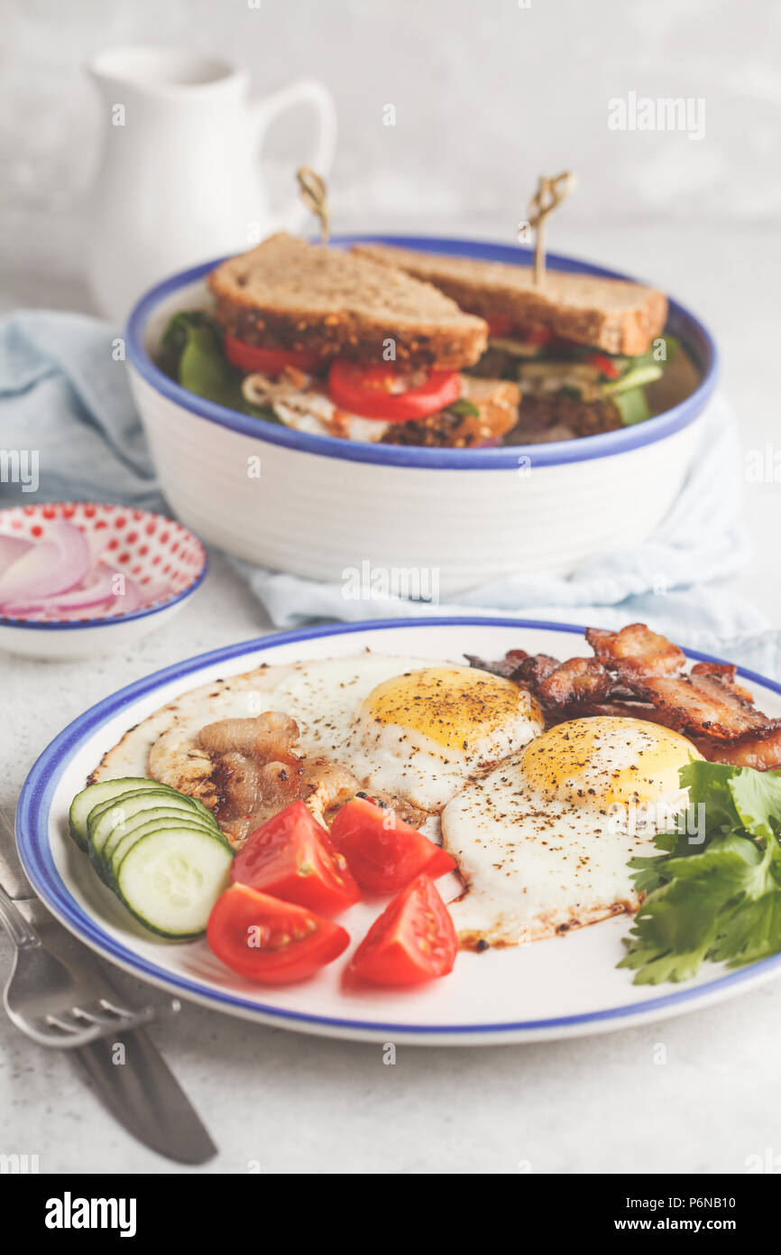Oeufs au plat avec du bacon et un sandwich avec de la viande, du fromage et des légumes. Délicieux petit déjeuner. Banque D'Images