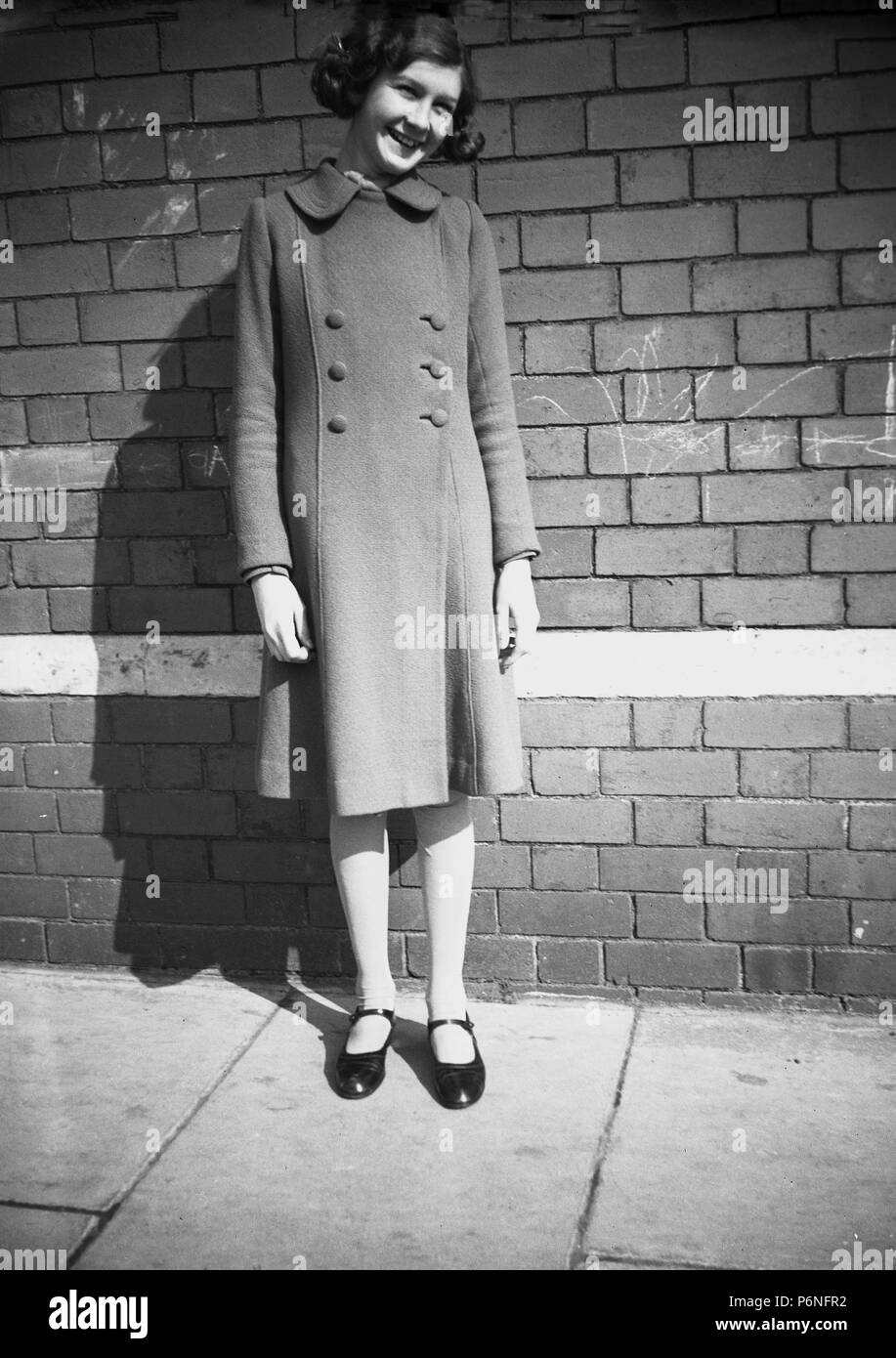 Années 1950, jeune fille à l'extérieur dans la rue weaing son manteau, England, UK. Banque D'Images