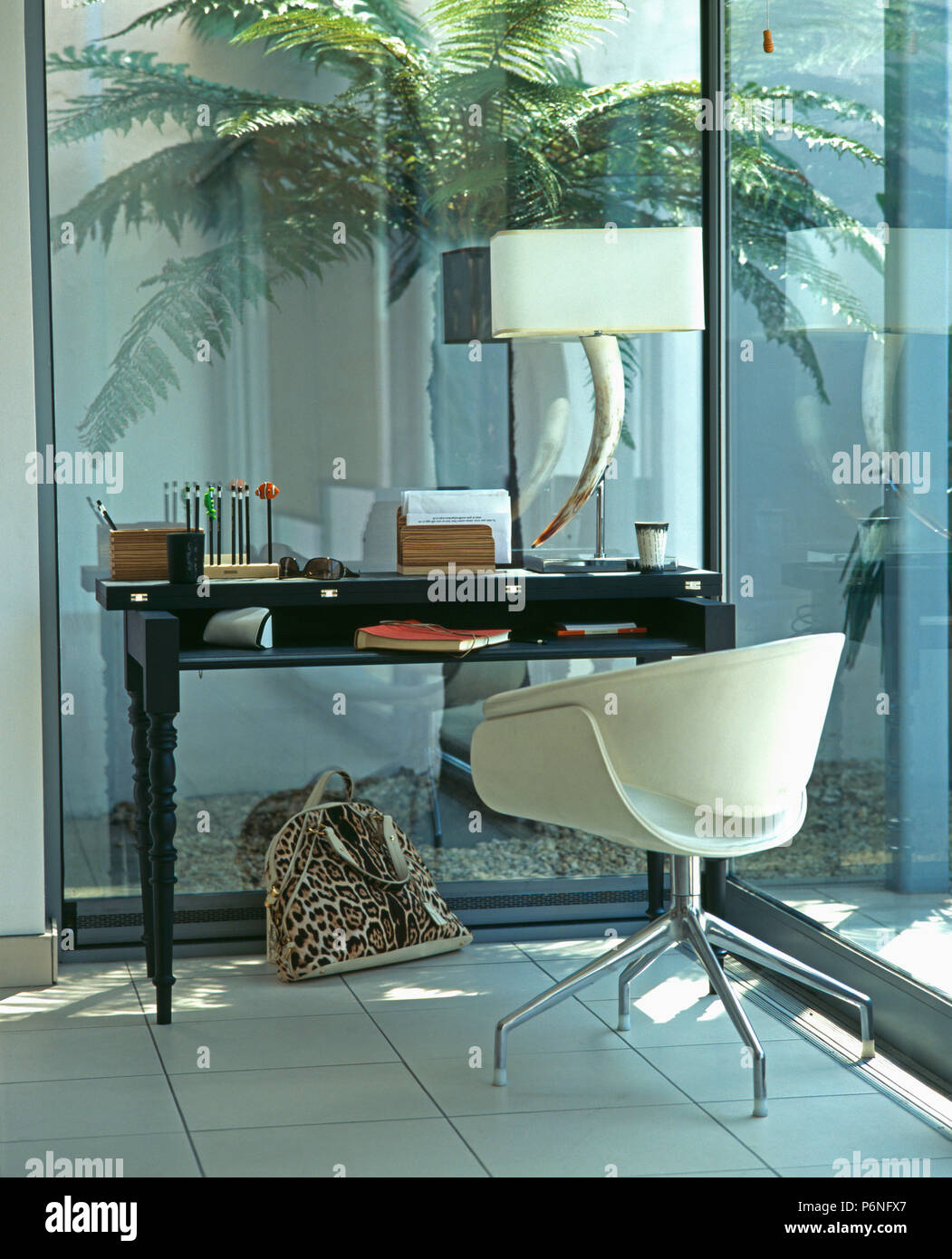 En plastique préformé blanc et chrome fauteuil à petit bureau avec lampe inhabituelle dans l'étude moderne avec des murs de verre Banque D'Images