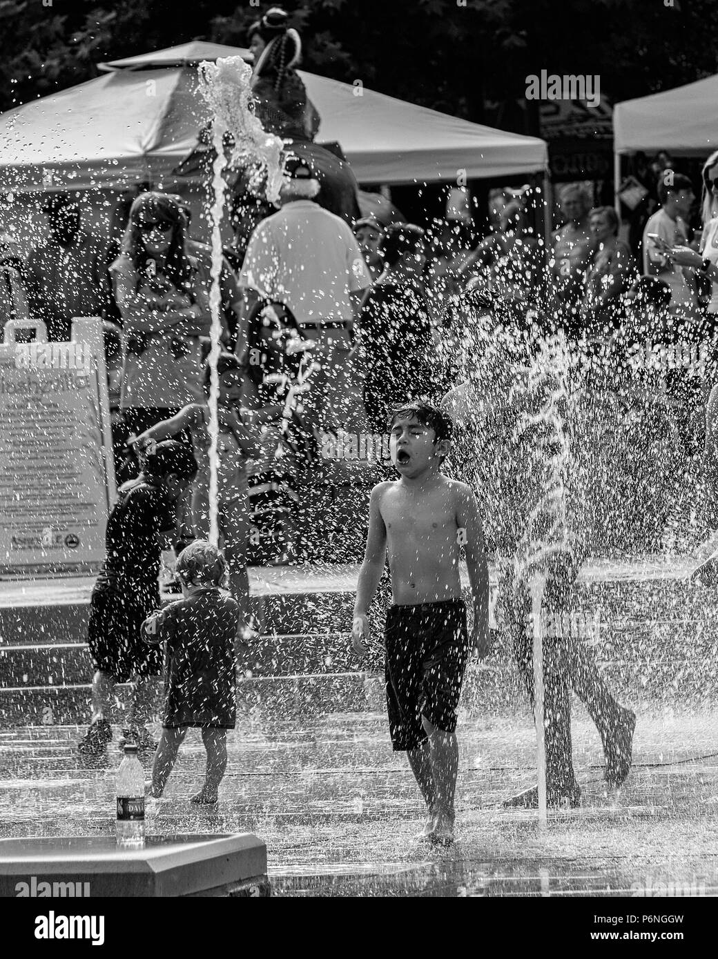 Un garçon hurle en voyant l'eau froide dans les fontaines de Splashville au centre-ville de Asheville, NC, USA Banque D'Images