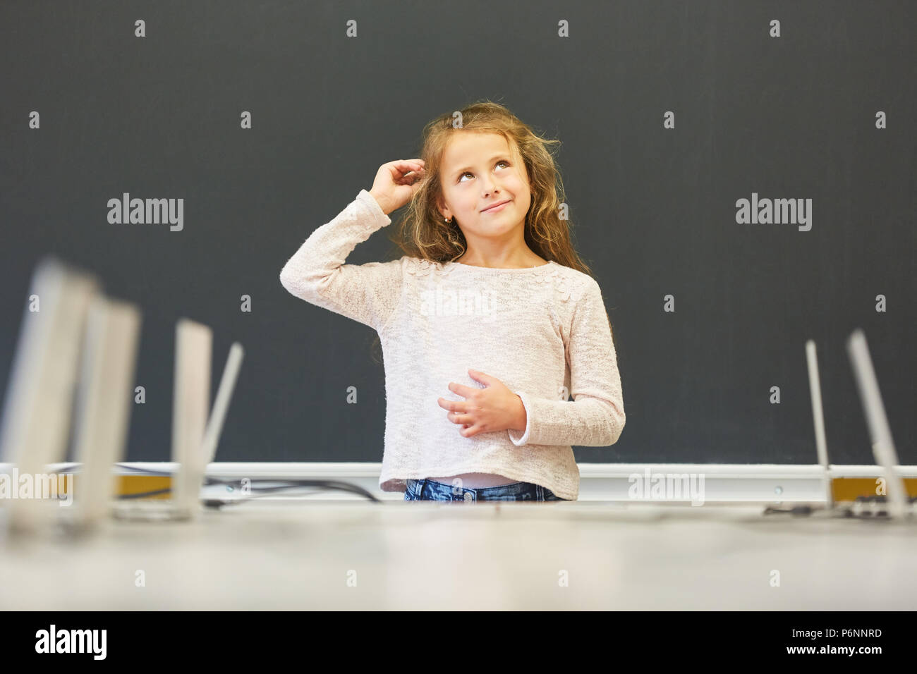 Jeune fille comme un étudiant pense à la solution au tableau noir de l'école élémentaire Banque D'Images