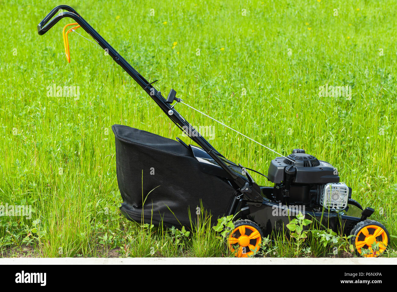 Tondeuse à essence moderne se dresse sur l'herbe verte fraîche, photo gros plan, Vue de côté Banque D'Images