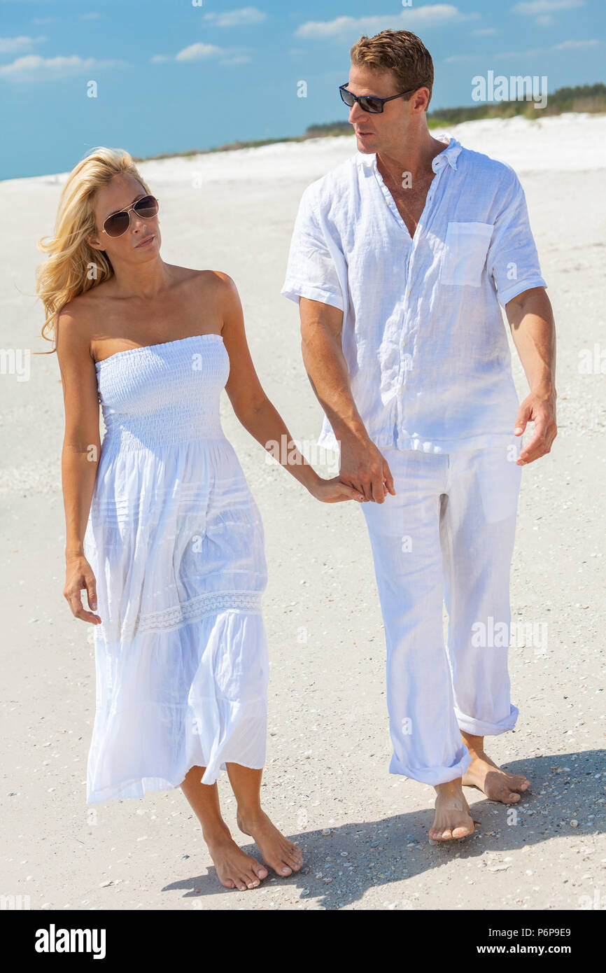 Réfléchis bien triste l'homme et la femme en couple romantique des vêtements blancs et des lunettes de soleil se tenant la main en marchant sur une plage tropicale déserte avec ciel bleu clair, r Banque D'Images